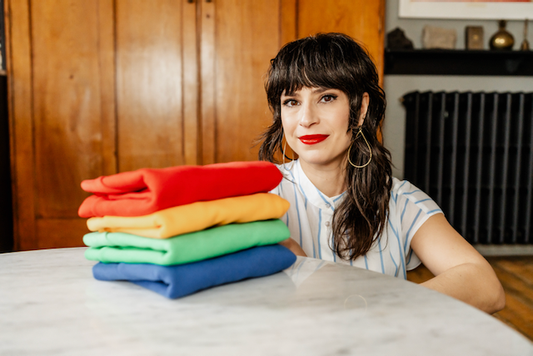 Elizabeth sitting behind a table with fold Hues Clothing. 